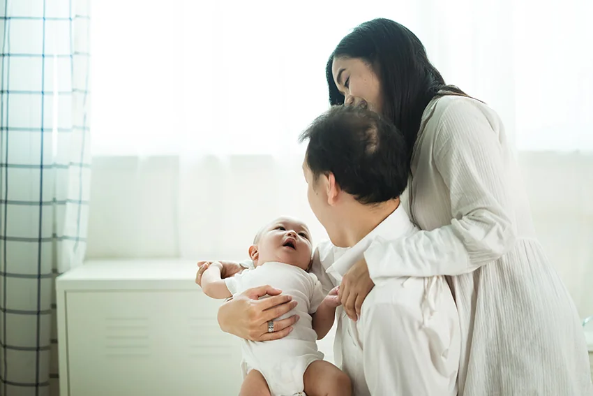 Asian parents playing with newborn baby in bedroom