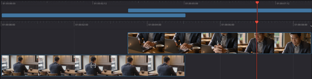 A video editing timeline interface with two video tracks and two audio/effect tracks. The top video track shows a man working on a laptop, and the bottom track shows a man from behind looking out a window. A red playhead marks the current position.