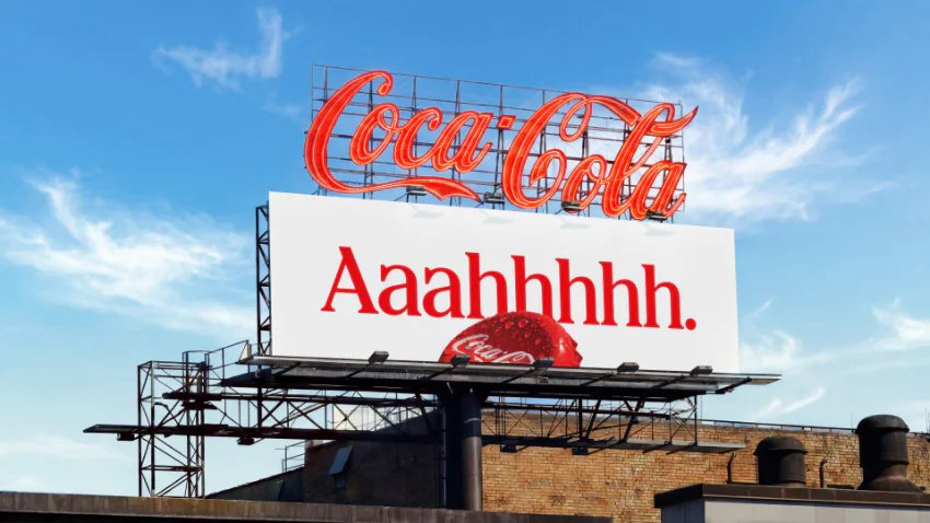 A Coca-Cola billboard against a blue sky, showing the red Coca-Cola logo, the word "Aaaahhhh." in red, and a large red strawberry-like object with a Coca-Cola logo.