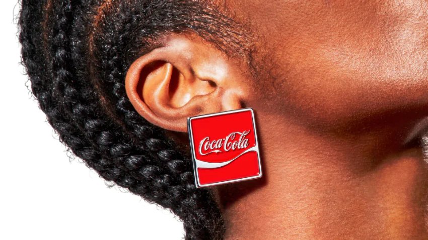 Close-up of a person's ear wearing a square red Coca-Cola logo stud earring.