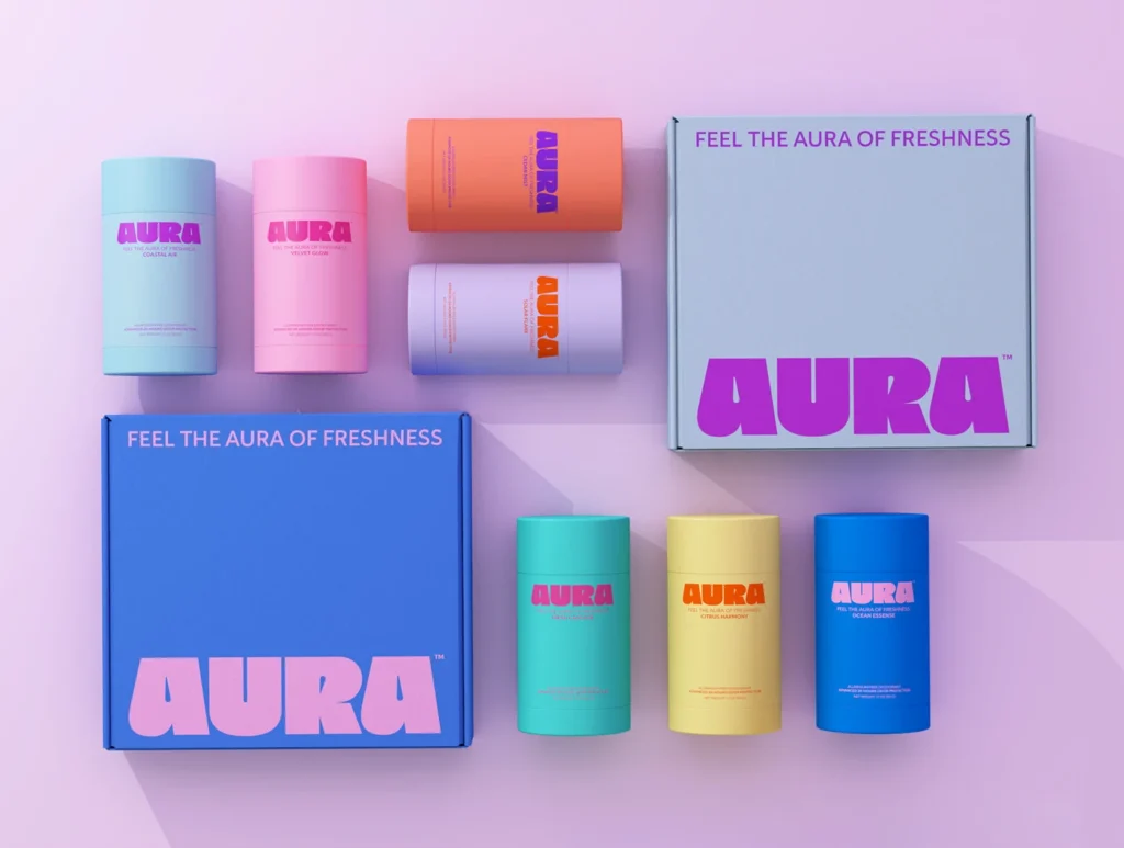 A colorful collection of Aura brand deodorant sticks and two branded boxes on a pink background.